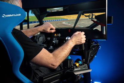 Person using a racing simulator with hands on a steering wheel, seated in a blue racing seat.